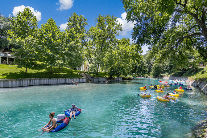 People on inter tubes floating on the Comal River on a sunny day.
