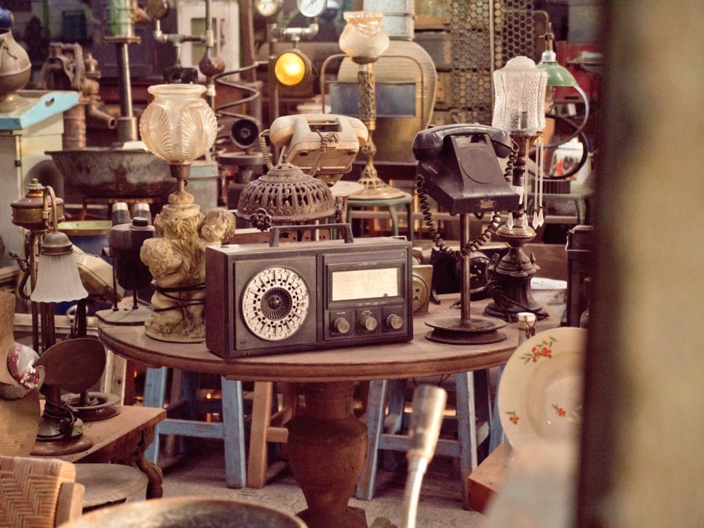 Antique phones, lamps, and radios sitting on tables. 
