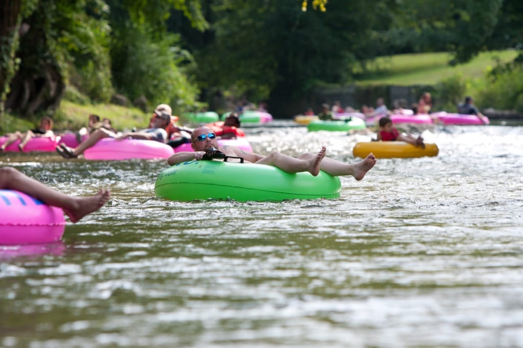 People lounging on assorted colors of inter tubes floating on a river.